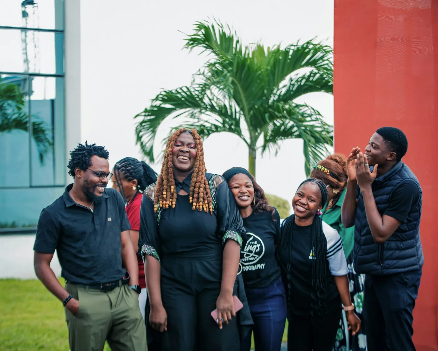 A group of young people laughing together outdoors beside a palm tree